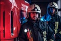 Two firemen wearing protective uniform standing next to a fire truck in a garage of a fire department. Royalty Free Stock Photo