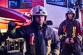 Two brave firemen wearing a protective uniform standing next to a fire truck. Royalty Free Stock Photo