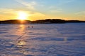 Two fishermen on a frozen lake catch fish in a hole of ice on the background of evening sunset. Winter arrives, bodies of water