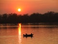 Two fishermen, a man and a woman, swim in a motor boat on the river against the background of an orange sunset. Romantic Royalty Free Stock Photo