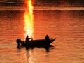 Two fishermen, a man and a woman, swim in a motor boat on the river against the background of an orange sunset. Romantic Royalty Free Stock Photo