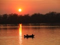 Two fishermen, a man and a woman, swim in a motor boat on the river against the background of an orange sunset. Romantic Royalty Free Stock Photo