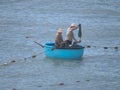 Two fishermen sail in a traditional Vietnamese boat. One of them throws the net