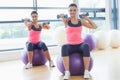 Two fit women exercising with dumbbells on fitness balls Royalty Free Stock Photo