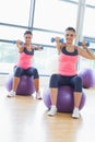 Two fit women exercising with dumbbells on fitness balls Royalty Free Stock Photo