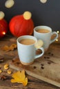 Two flavored pumpkin coffee with spices in ceramic cups on a wooden table with orange pumpkins in the background. Bokeh.
