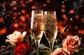 Two flute glasses with sparkling champagne roses on red pink golden background with golden bokeh lights confetti glitter. Royalty Free Stock Photo