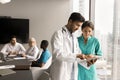 Two focused diverse doctor colleagues using tablet on corporate meeting