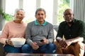 Two focused diverse senior couple and their african american male friend watching tv and having fun