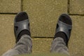 Two foots of a person in socks in flip flops. Black socks standing on stone floor.