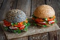 Two fresh appetizing hamburgers dark and light with sesame seeds, close-up, with fresh vegetables tomato, sweet pepper,