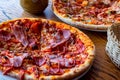 Two fresh baked homemade sliced pizzas with cheese and ham topping served with kitchenware on wooden background. Royalty Free Stock Photo