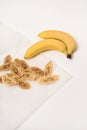 Two fresh bananas, next to which are dried banana slices on parchment paper. White background. Royalty Free Stock Photo