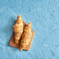 Two fresh croissants, wooden cutting board on blue background. Top view