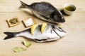 Two fresh fish Dorada with bay leaves, some pieces of lemon, a bowl of oil and some spices on a wooden table Royalty Free Stock Photo