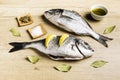 Two fresh fish Dorada with bay leaves, some pieces of lemon, a bowl of oil and some spices on a wooden table Royalty Free Stock Photo