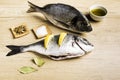 Two fresh fish Dorada with bay leaves, some pieces of lemon, a bowl of oil and some spices on a wooden table Royalty Free Stock Photo