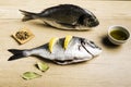 Two fresh fish Dorada with bay leaves, some pieces of lemon, a bowl of oil and some spices on a wooden table Royalty Free Stock Photo