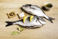 Two fresh fish Dorada with bay leaves, some pieces of lemon, a bowl of oil and some spices on a wooden table Royalty Free Stock Photo