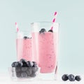 Two fresh purple milkshakes with blueberries in bowl, striped straws closeup on soft light mint color background and white wood. Royalty Free Stock Photo