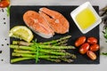 Two fresh raw salmon steaks with vegetables and spices: asparagus, tomatoes, peppercorns, rucola, lemon and olive oil on gray back Royalty Free Stock Photo