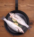 Two fresh sea bass fish on frying pan with ingredients Royalty Free Stock Photo