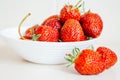 Two fresh strawberries lying on a table next to a plate of strawberries Royalty Free Stock Photo