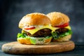 Two fresh tasty homemade hamburgers with fresh vegetables, lettuce, tomato, cheese beside sliced tomatoes on a cutting board. Free