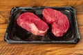 Two fresh uncooked fillet steaks on a black plastic tray.