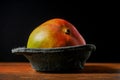 Two fresh whole mango fruit in a black plastic container on a wooden surface, Royalty Free Stock Photo
