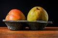 Two fresh whole mango fruit in a black plastic container on a wooden surface Royalty Free Stock Photo