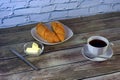 Two freshly baked croissants on a white ceramic plate and a cup of black coffee on a saucer with a spoon and butter with a knife Royalty Free Stock Photo