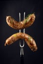 Two fried beef sausages on a fork. The concept of a delicious lunch for a hotel on a black background Royalty Free Stock Photo