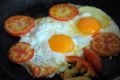 Two fried eggs in black frying pan and slices tomato. Process of cooking