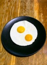 two fried eggs on black plate on wooden table Royalty Free Stock Photo