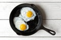 Two fried eggs in cast iron frying pan sprinkled with ground black pepper. Isolated on white painted wood from above. Royalty Free Stock Photo