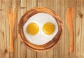 Two fried eggs on wooden plate, knife and fork on wooden table Royalty Free Stock Photo