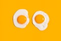 Two fried sunny-side-up eggs with bright glossy yoke on yellow background. Culinary food concept