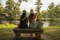 two friend girls with hats chatting sitting on a stone bench in front of the river Royalty Free Stock Photo