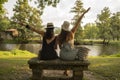 two friend girls with hats chatting sitting on a stone bench in front of the river Royalty Free Stock Photo