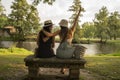 two friend girls with hats chatting sitting on a stone bench in front of the river Royalty Free Stock Photo