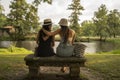 two friend girls with hats chatting sitting on a stone bench in front of the river Royalty Free Stock Photo