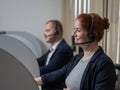 Two friendly call center employees answer customers by phone. Man and woman woman talking on a headset in the office. Royalty Free Stock Photo
