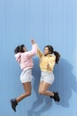 Two friendly girls jumping and clapping their hands in the air on a blue background Royalty Free Stock Photo
