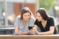 Two friends checking smart phone content in a park Royalty Free Stock Photo