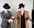 Two friends dressed in vintage clothes and depict retro detectives and spies in English classic style on a white studio background