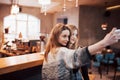 Two friends drinking coffee in a cafe, taking selfies with a smart phone and having fun making funny faces. Focus on the Royalty Free Stock Photo