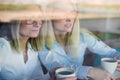 Two friends are enjoying coffee in a coffee shop, looking through a glass with reflections, sitting at a table chatting Royalty Free Stock Photo
