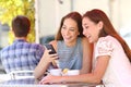 Two friends or family sharing a smart phone in a coffee shop Royalty Free Stock Photo