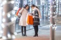 Two friends meet in front of a shopping center looking at gifts inside their bags that they bought for Christmas Royalty Free Stock Photo